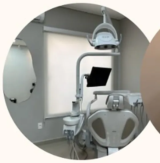 Consultório da Dra. Natália: cadeira odontológica clara, janela com persiana e espelho orgânico na parede